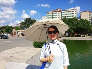 中国昆明市にある昆明市博物館の前で、チャイナ服を着たレイレイが日傘をさして笑っている写真。