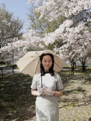 桜が満開の公園でチャイナドレスを着て日傘をさしているレイレイ。