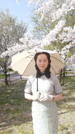 桜が満開の公園でチャイナドレスを着て日傘をさしているレイレイ。